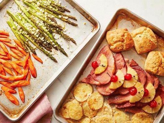 Easter dinner of ham, vegetables and a bun on two baking sheets