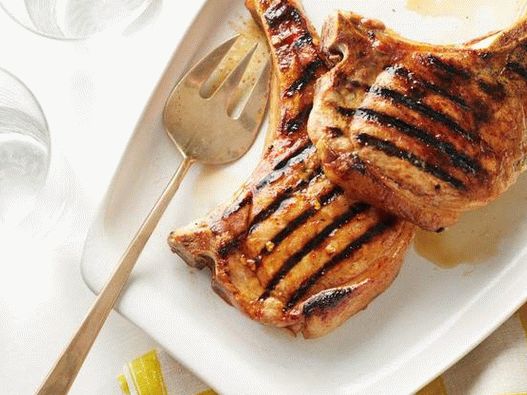 Photo of a pork chop on a bone in a sharp orange glaze